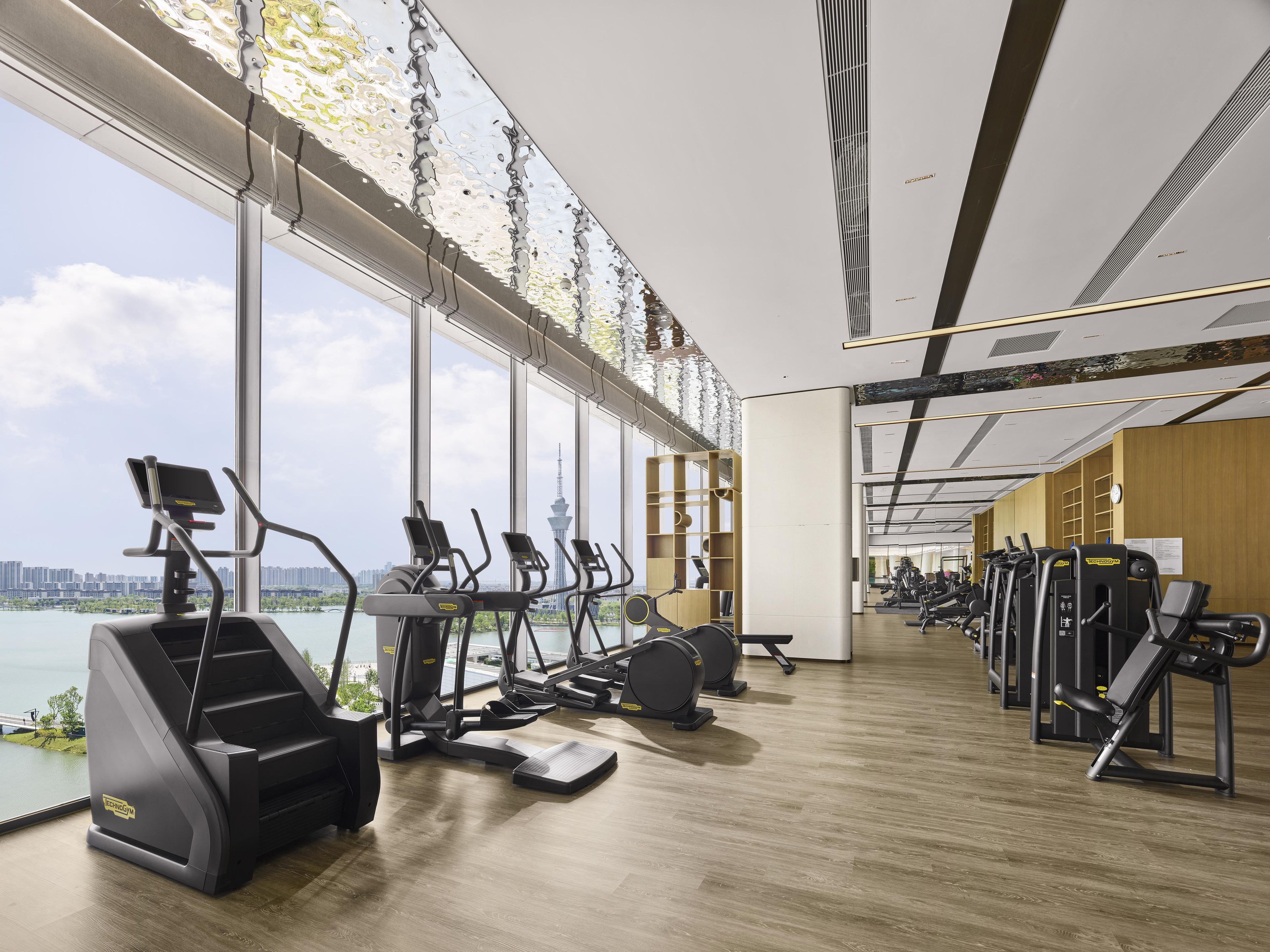 A gym with cardio machines, weight stations, and a view of a city skyline.