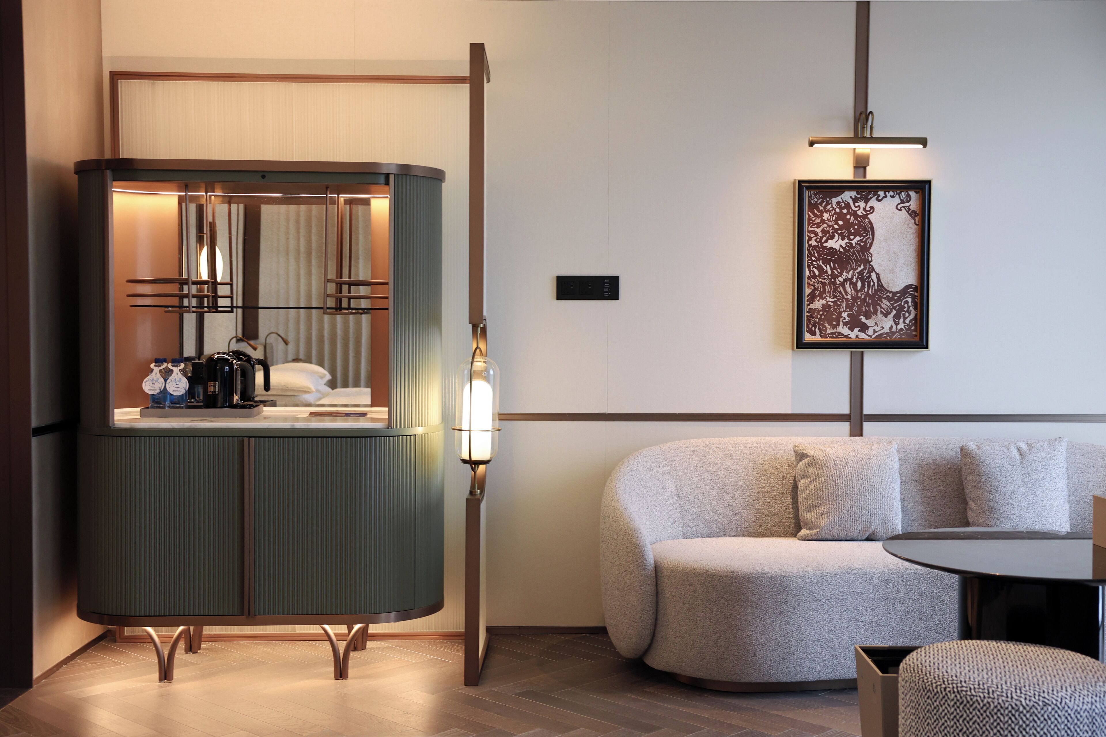 Una habitación de hotel moderna con un armario verde, una mesa redonda, un sofá y una obra de arte enmarcada en la pared.