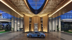 A modern hotel entrance with a blue sports car parked in front, a glass facade, and a ceiling with a light pattern. - Hilton Changshu (Suzhou)