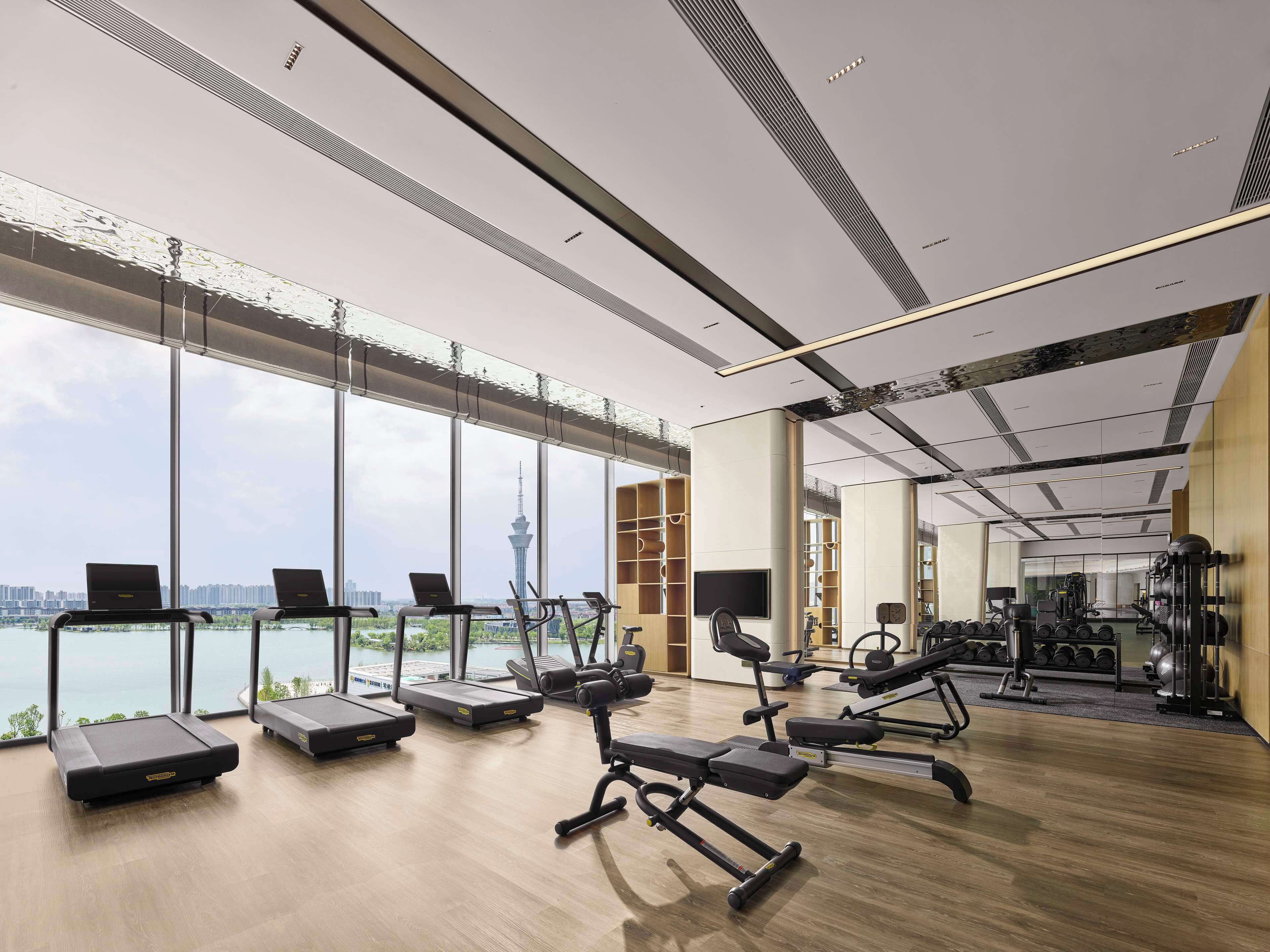 A modern gym with treadmills, weight machines, and a large window overlooking a cityscape.