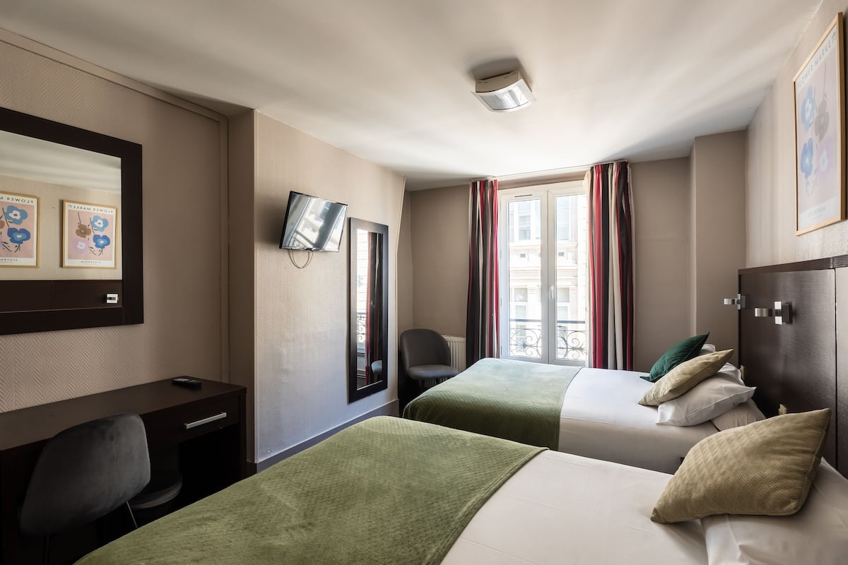 A hotel room with two beds, a desk, a chair, a TV, and a window with curtains.