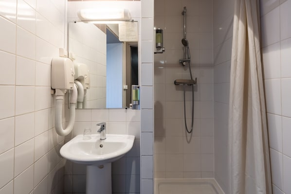 A bathroom with a white sink, a mirror, a handheld showerhead, and a toilet paper dispenser. - Hôtel Bristol Nord (Paris)