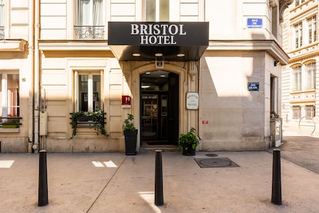 The exterior of the Bristol Hotel with a prominent sign, a double door entrance, and potted plants.