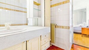 Un baño con lavamanos blanco, espejo y repisa de vidrio. Hay un radiador y suelo de madera.