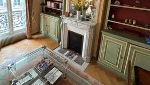 A living room with a fireplace, bookshelves, and a glass coffee table. - Pour un Élégant Séjour aux Invalides - Chevert (Paris)