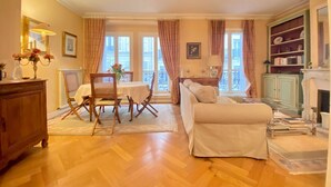 A living room with a sofa, a dining table with chairs, a fireplace, and a bookshelf. - Pour un Élégant Séjour aux Invalides - Chevert (Paris)