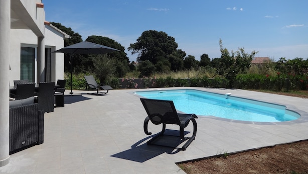 Een modern zwembadterras met ligbedden en een grote parasol.