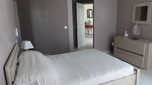 Een moderne slaapkamer met een houten bed, een nachtkastje met een lamp, een dressoir en een spiegel aan de muur.