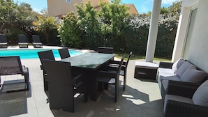 Een terras buiten met een zwembad, rieten meubilair en uitzicht op het omliggende groen.