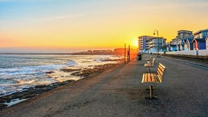 A beach with a row of benches, a promenade, and buildings in the background. - East Titchberry Cottage (Hartland)