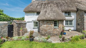 A traditional stone house with a thatched roof, a stone entrance, and a small garden with potted plants. - East Titchberry Cottage (Hartland)