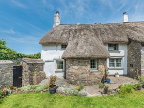 A traditional stone house with a thatched roof, a stone entrance, and a small garden with potted plants.
