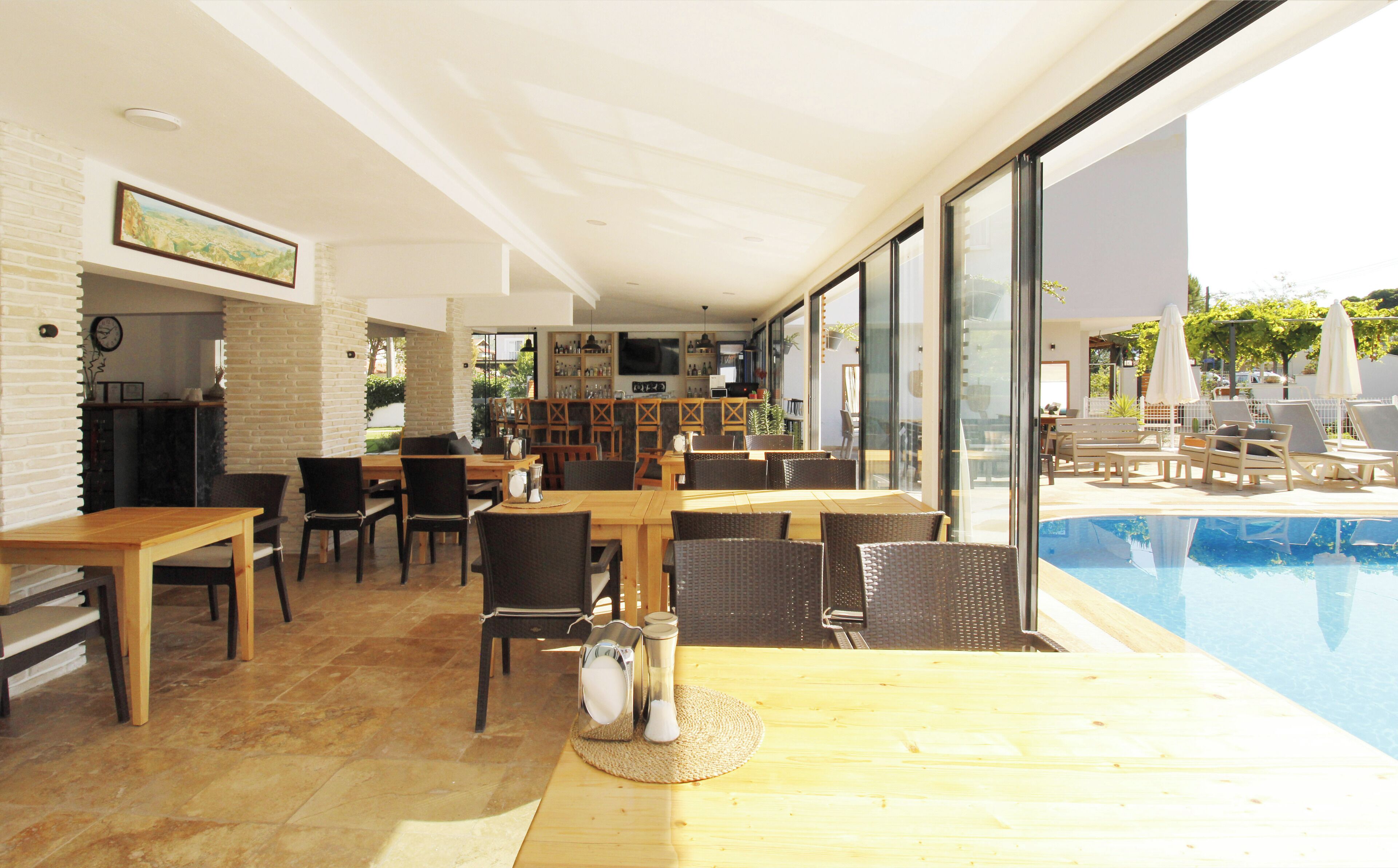 An indoor pool area with a wooden table and chairs, a bar area with shelves, and a view of the outdoor pool.