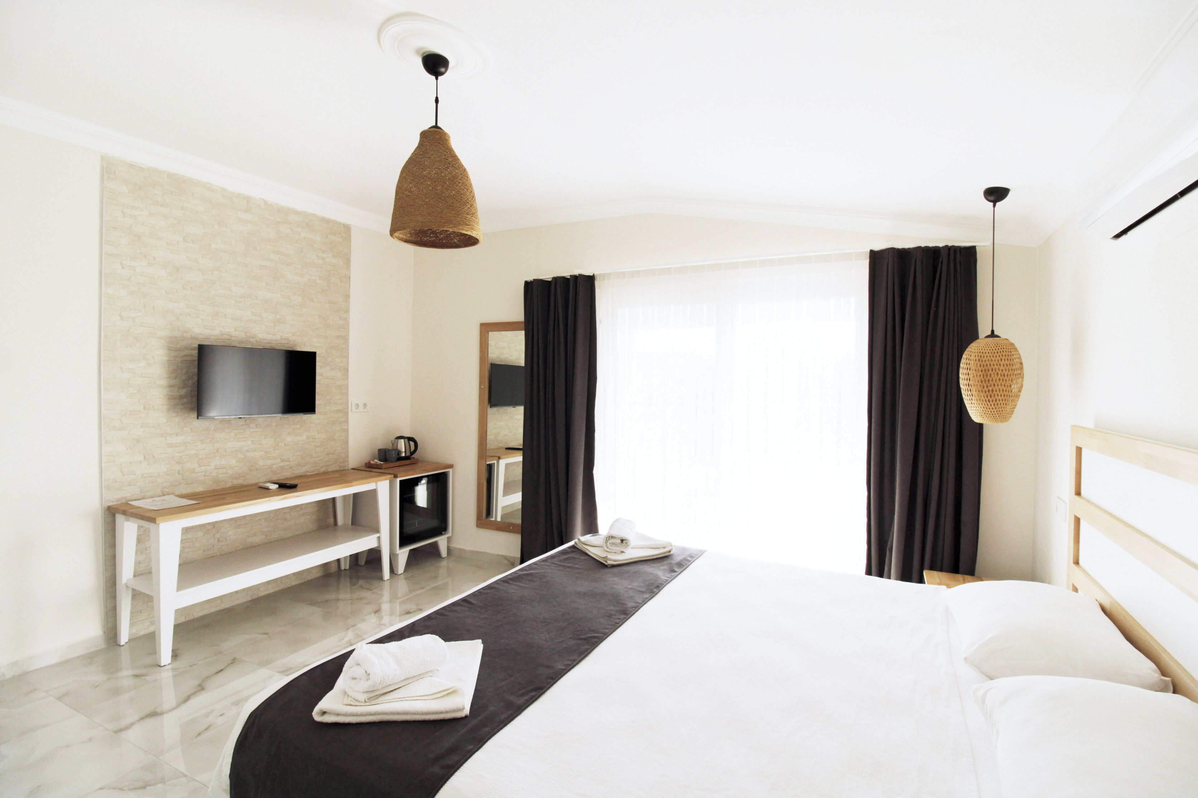 Une chambre d’hôtel moderne équipée d’un lit, d’un bureau, d’une télévision et d’une grande fenêtre avec des rideaux.