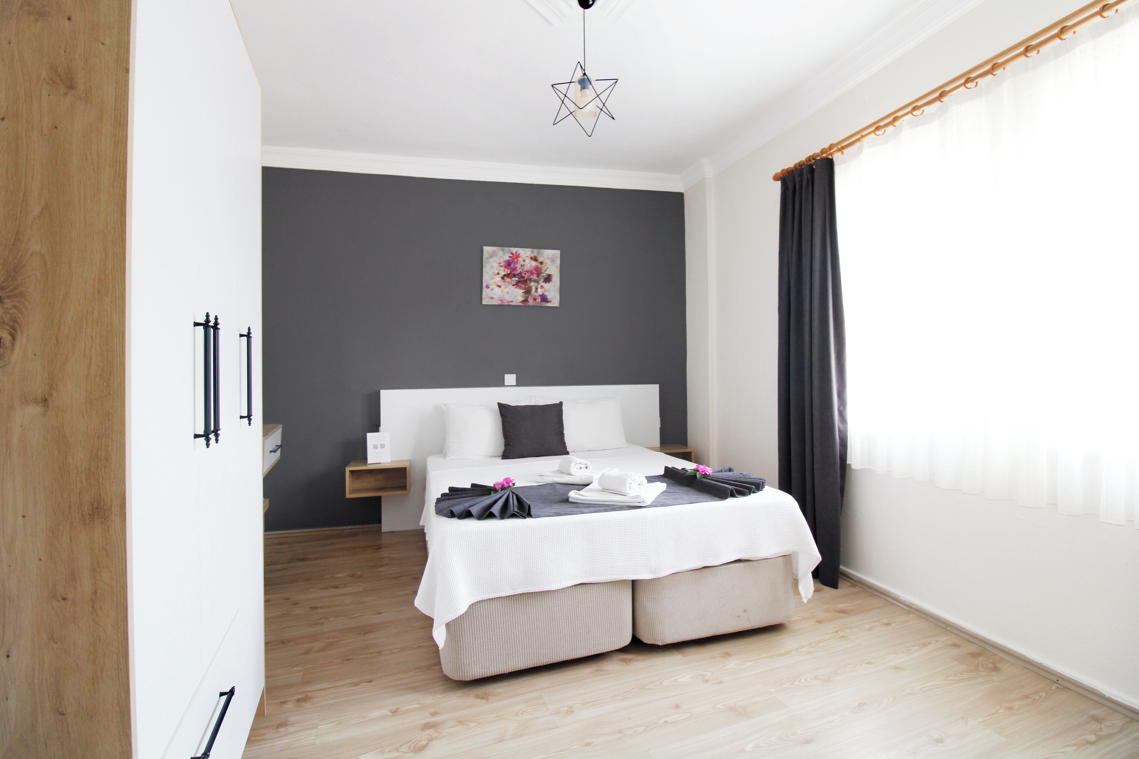 A modern bedroom with a large bed, a bedside table, a nightstand, a wall-mounted artwork, and a star-shaped ceiling light.
