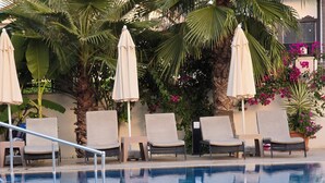 A swimming pool with lounge chairs and umbrellas, surrounded by greenery and flowers. - Tufan Boutique Hotel & Apart (Ortaca)