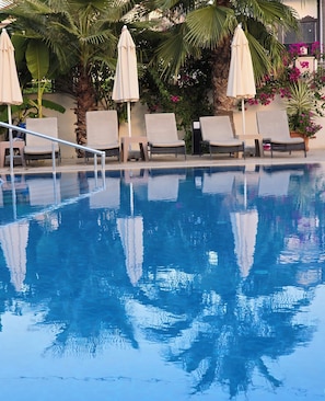 A swimming pool with lounge chairs and umbrellas, surrounded by greenery and flowers.