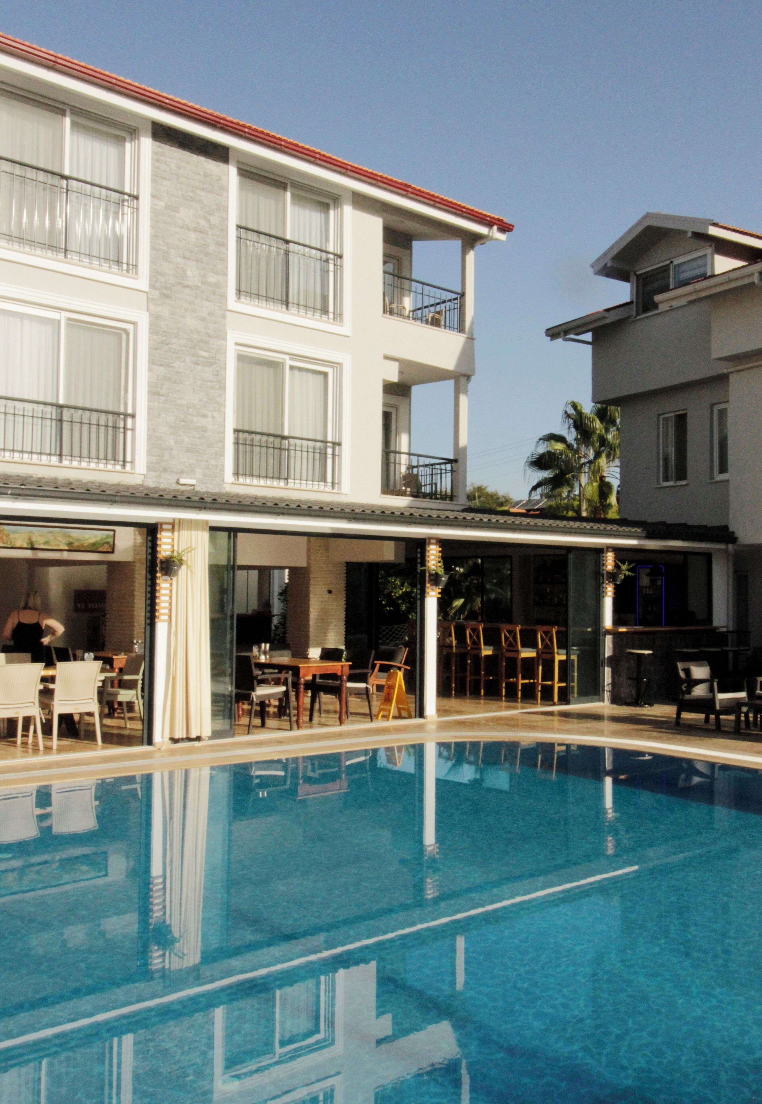A hotel with a swimming pool, outdoor seating, and a two-story building with balconies.