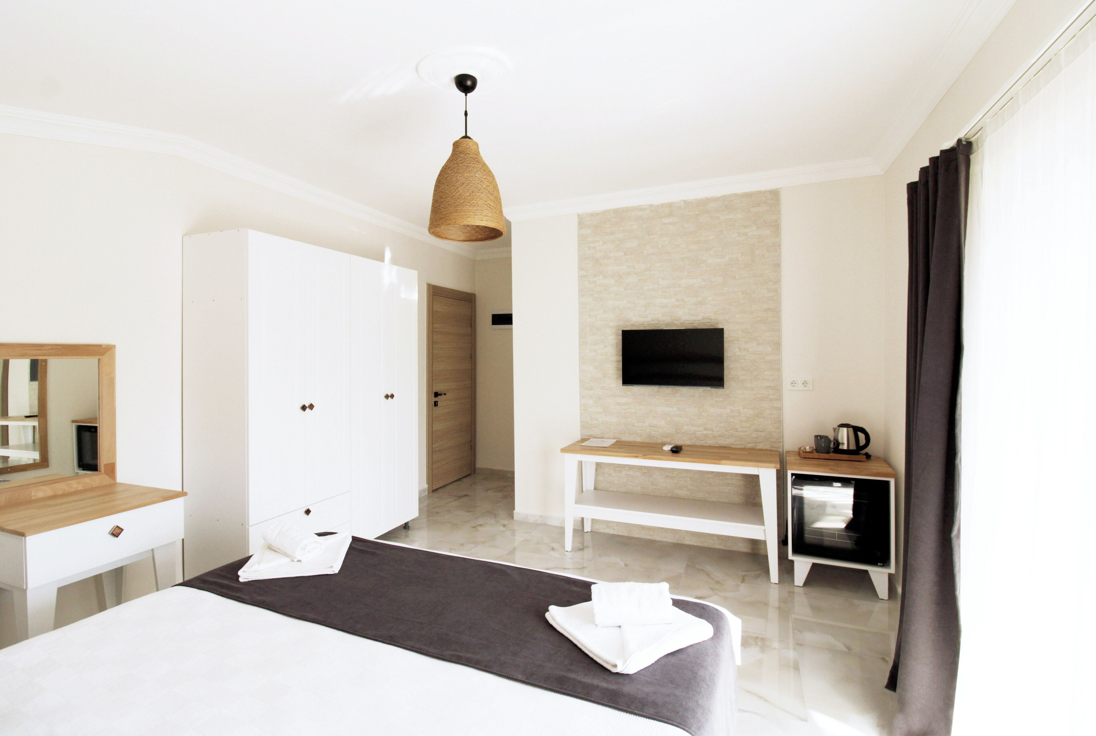 A modern hotel room with a bed, a desk, a TV mounted on the wall, and a wardrobe.
