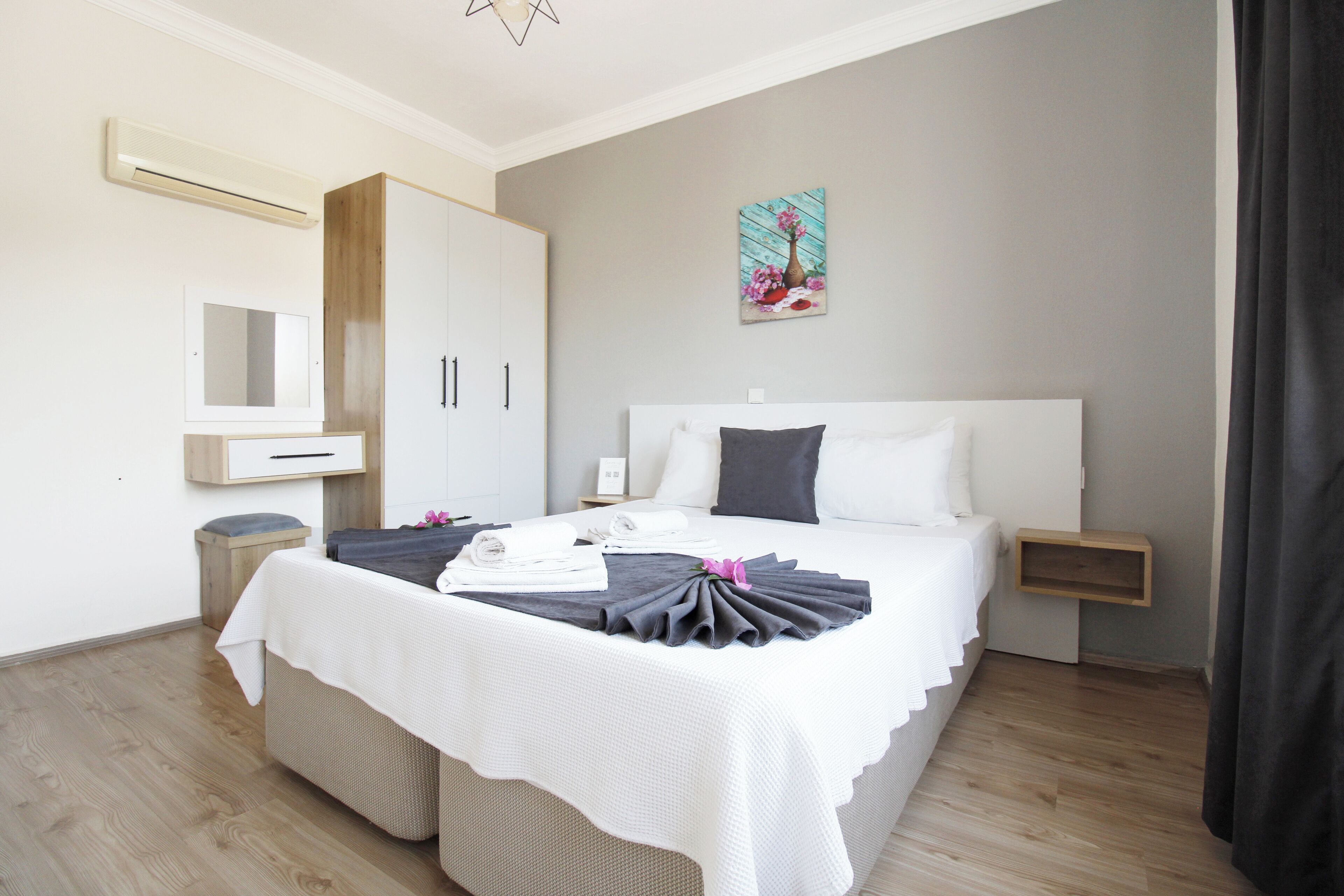 A modern hotel room with a large bed, a wardrobe, a mirror, and a painting on the wall.