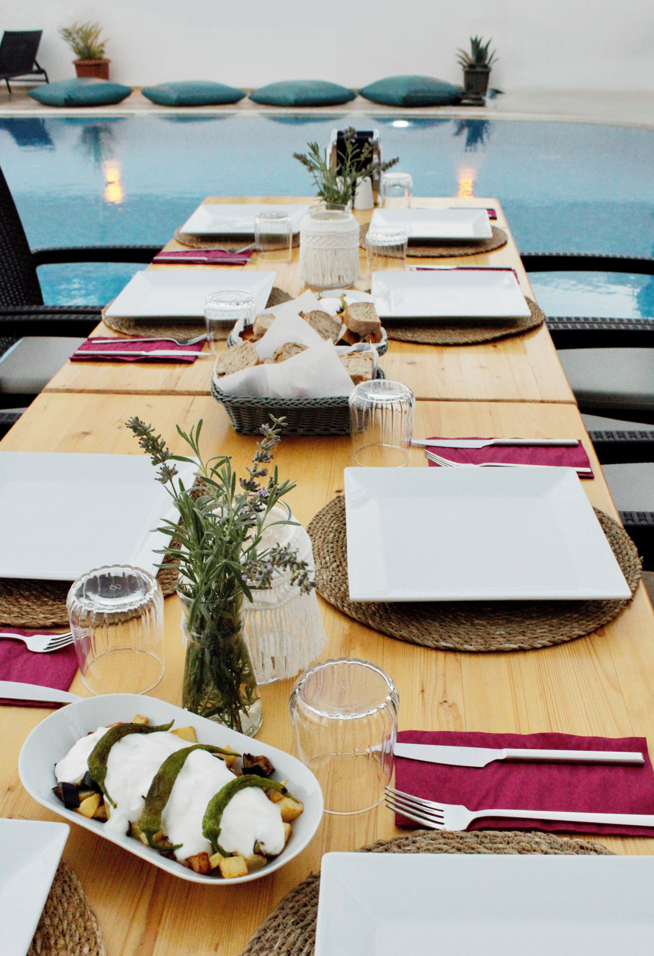 Une table à manger dressée avec des assiettes, des couverts et un plat rempli de nourriture, donnant sur une piscine.