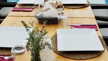 Una mesa de comedor preparada con platos, cubiertos y un tazón de comida, con vistas a una piscina.