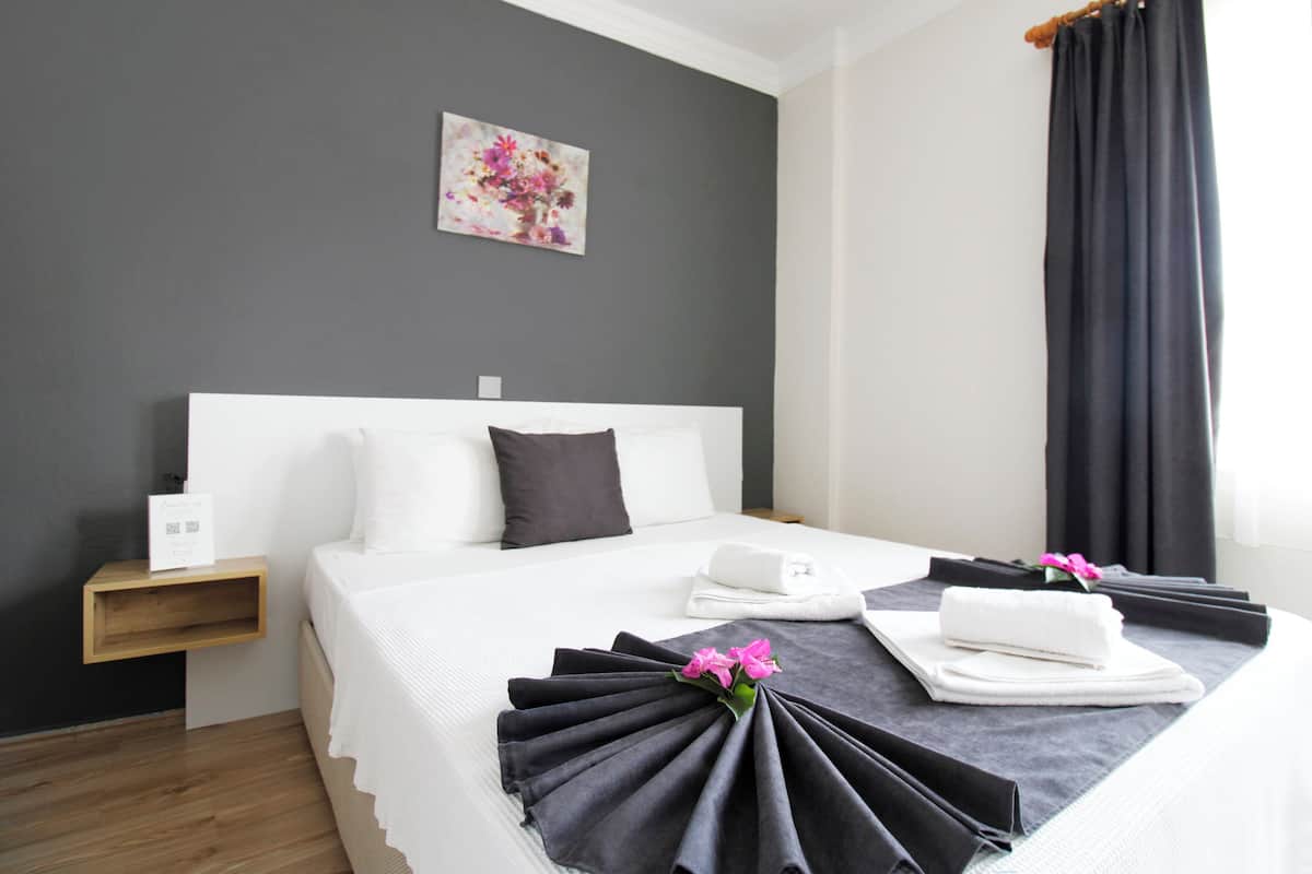 Une chambre d’hôtel avec un lit bien fait, une table de chevet, une œuvre d’art accrochée au mur et une fenêtre avec des rideaux.