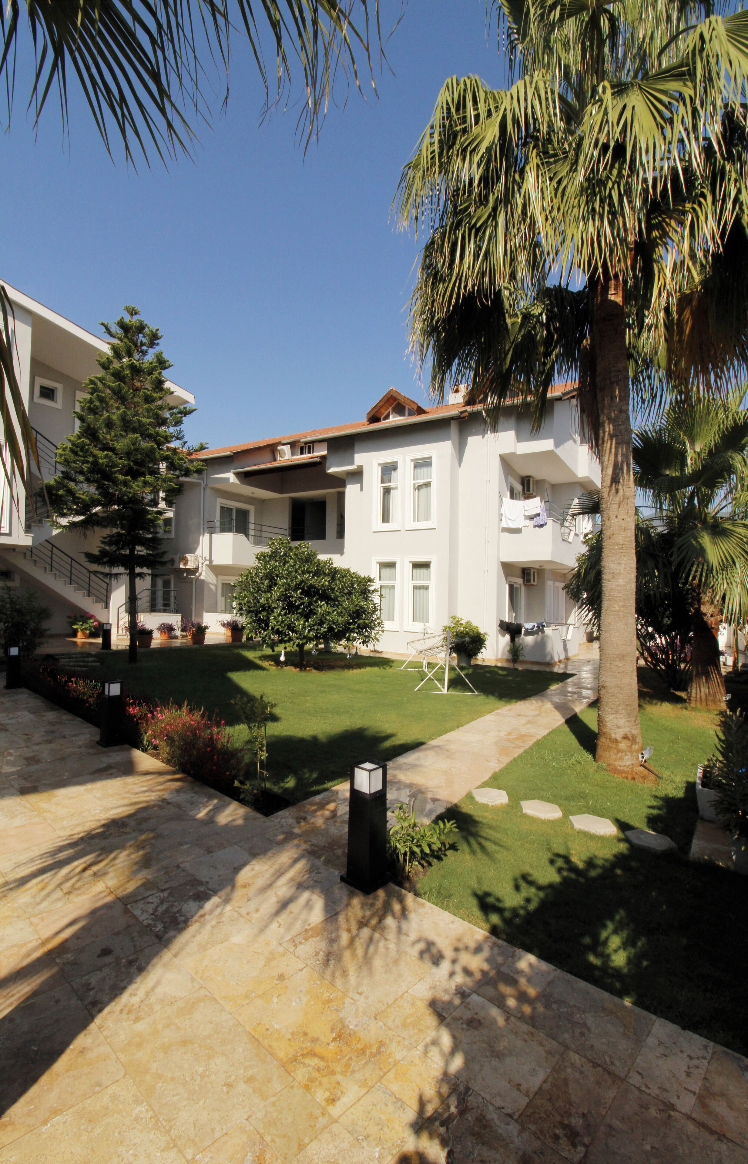 A multi-story building with balconies, a well-maintained lawn, and a palm tree.