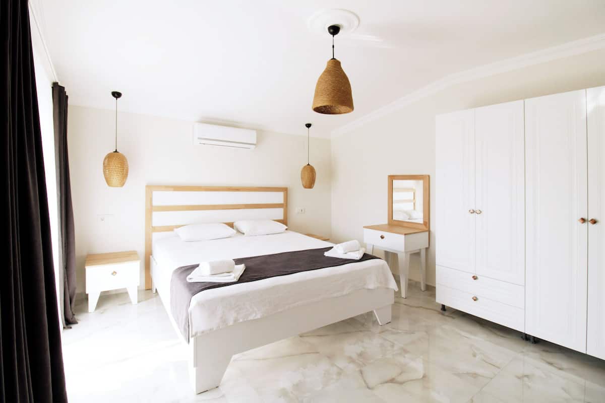 Une chambre d’hôtel comprenant un lit, des tables de chevet, un bureau, une armoire et des lampes suspendues.