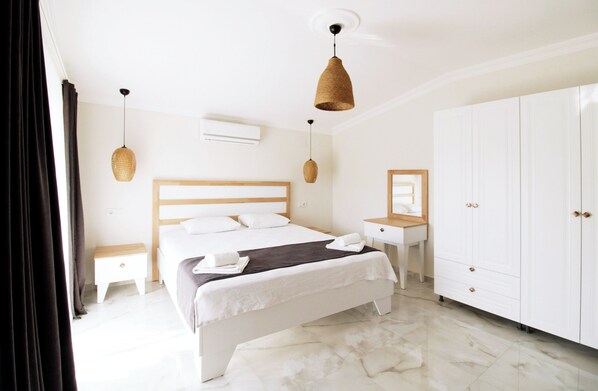 Quarto de hotel com cama, mesas de cabeceira, escrivaninha, guarda-roupa e luminárias pendentes.
