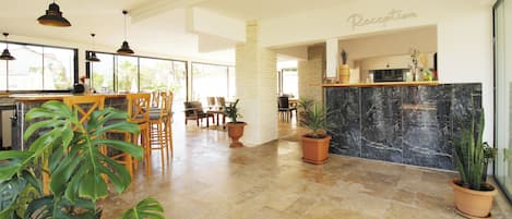 Amplia zona de recepción con mostrador de mármol, sillas de madera y plantas en macetas.
