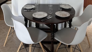 A dining area with a round table set for four, surrounded by white chairs. A framed artwork is mounted on the wall above the table. - Tinos - House - Sleeps 5 - Pet Friendly - Parking (Tinos)