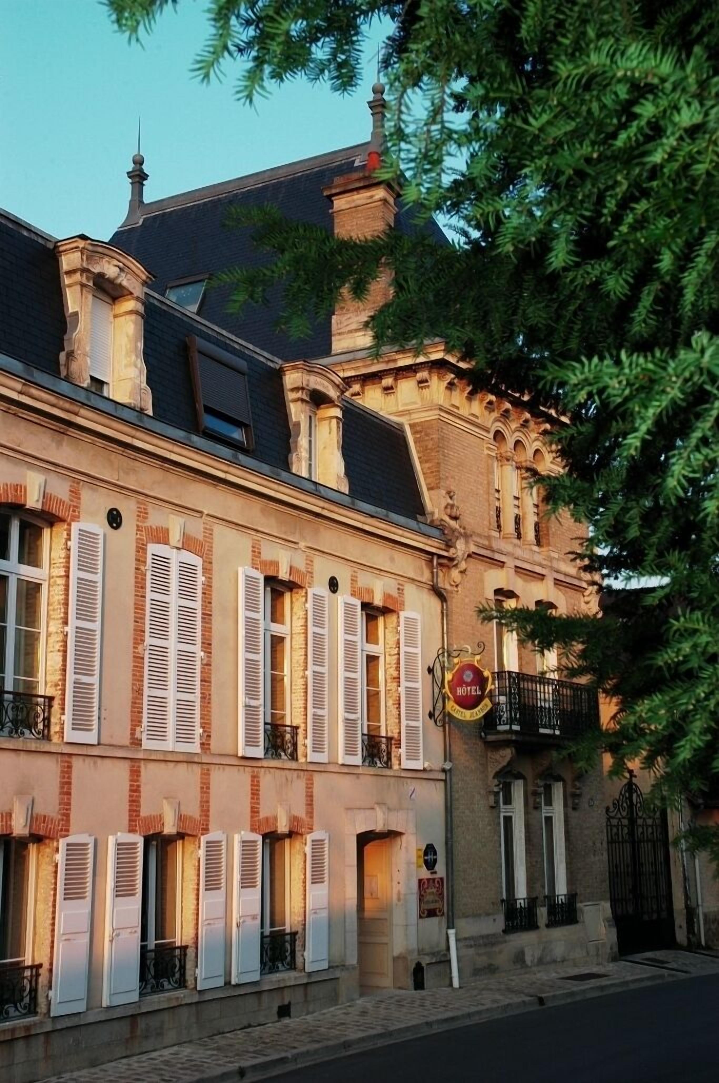 A historic building with multiple windows and shutters, a balcony, and a sign indicating it is a hotel.