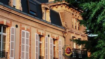 A historic building with multiple windows and shutters, a balcony, and a sign indicating it is a hotel.