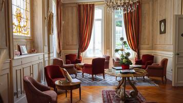 A room with a chandelier, red upholstered chairs, a wooden coffee table, and a patterned rug.
