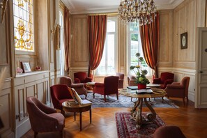 A room with a chandelier, red upholstered chairs, a wooden coffee table, and a patterned rug. - Hotel Castel Jeanson (Aÿ-Champagne)