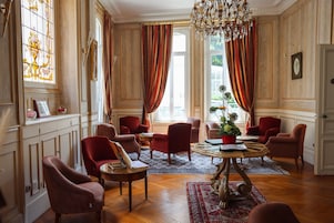 Una habitación con candelabro, sillas tapizadas en rojo, una mesa de centro de madera y una alfombra estampada.