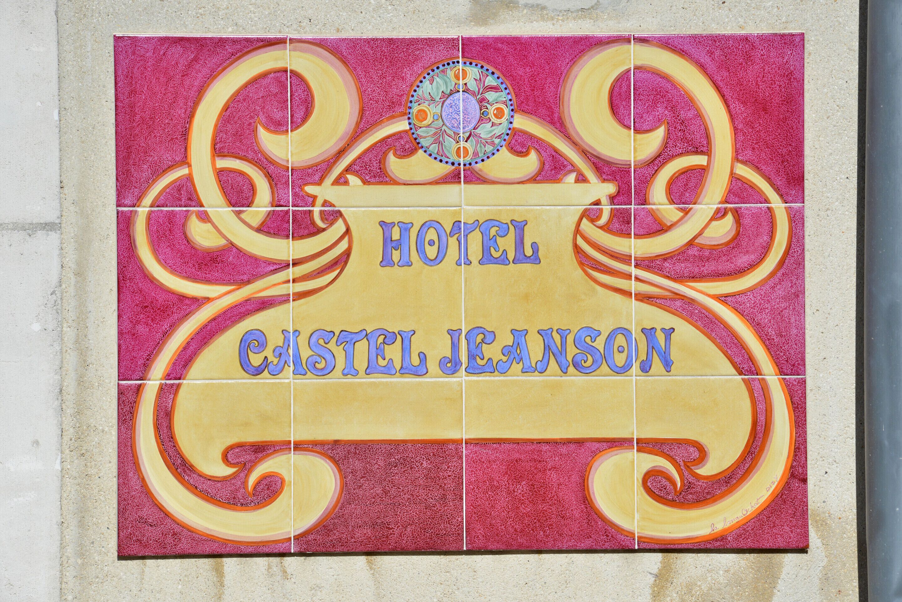 Ein blau beschriftetes Schild mit den Wörtern „HOTEL“ und „CASTEL JEANSON“, umgeben von dekorativen Spiralen und einem zentralen Wappen.