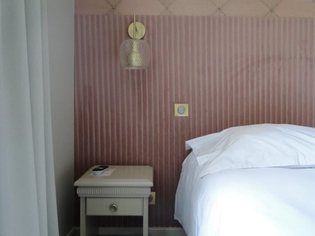 A bedroom with a bed, a nightstand, a lamp, and a wall-mounted light fixture.