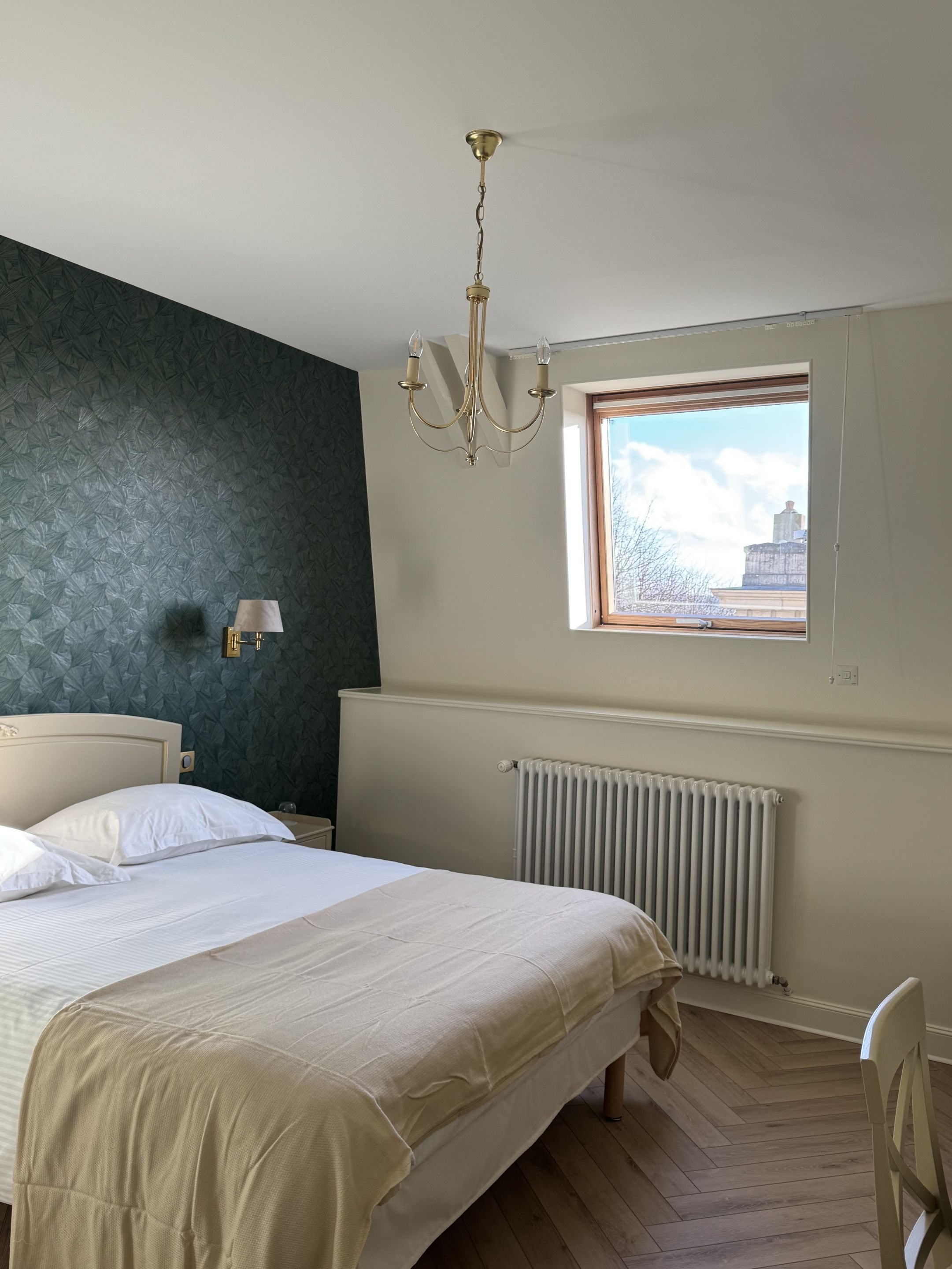 Een slaapkamer met een bed, een radiator, een raam en een kroonluchter.