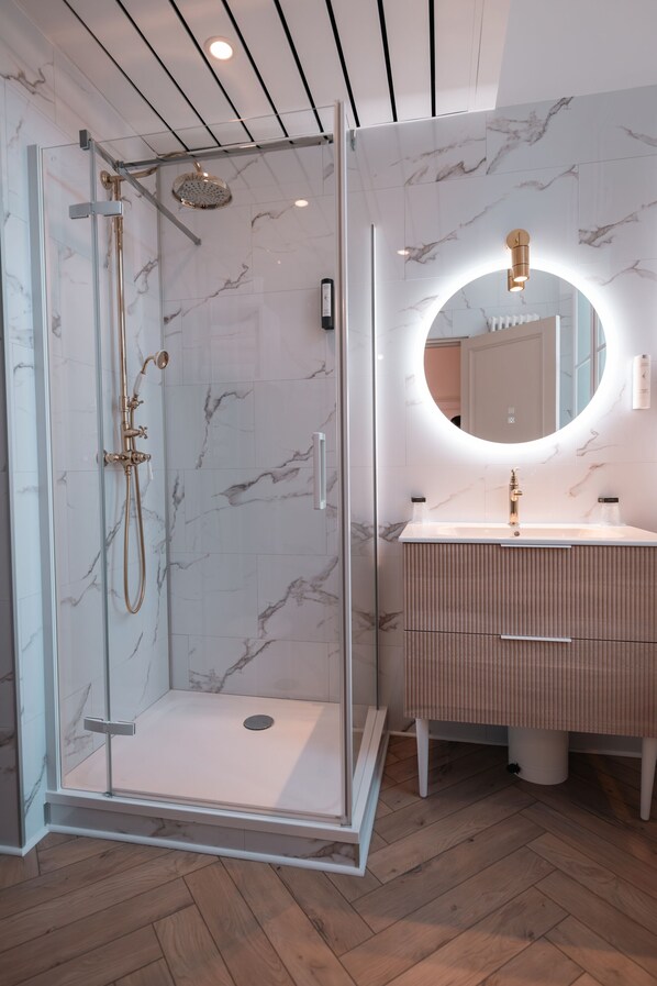 Un baño moderno con cabina de ducha de vidrio, tocador con salpicadero de mármol y espejo redondo con iluminación integrada.