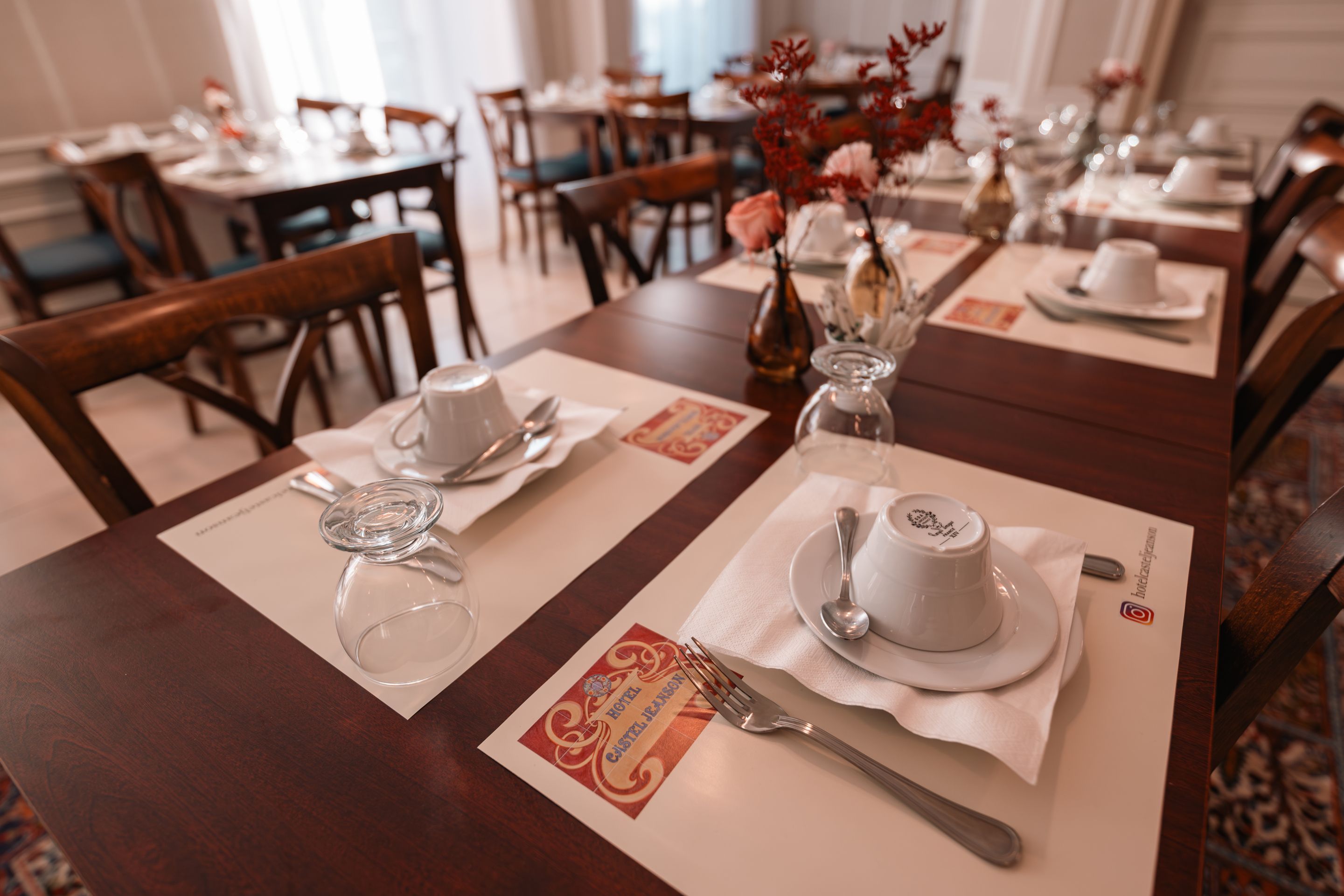 A dining table set with a white plate, a cup, a spoon, and a glass.