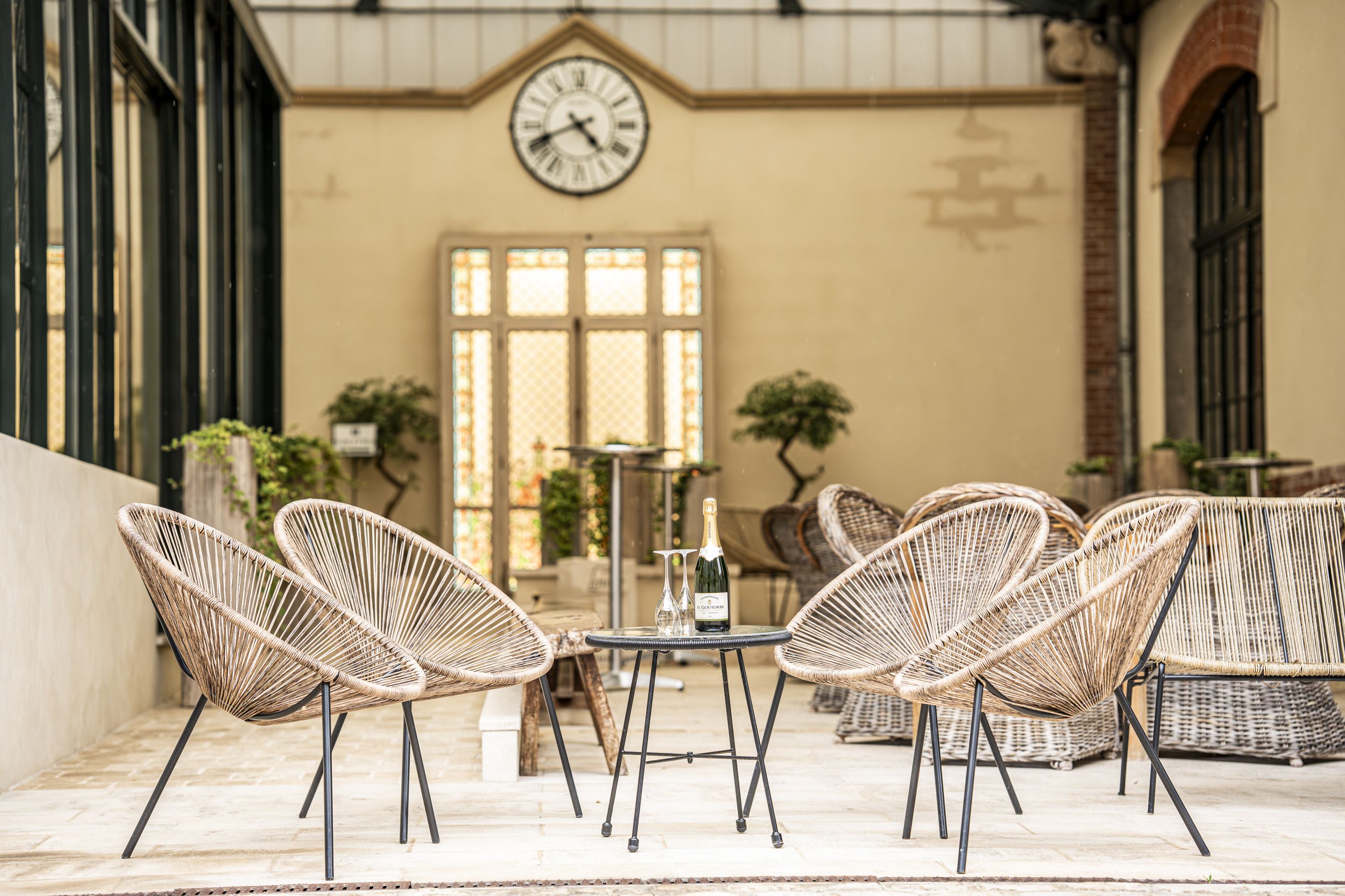 Una terraza con sillas de mimbre, una mesa y un reloj en la pared.