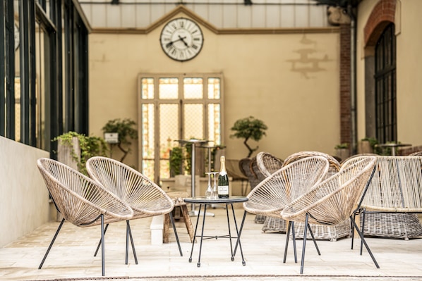 A terrace with wicker chairs, a table, and a clock on the wall. - Hotel Castel Jeanson (Aÿ-Champagne)