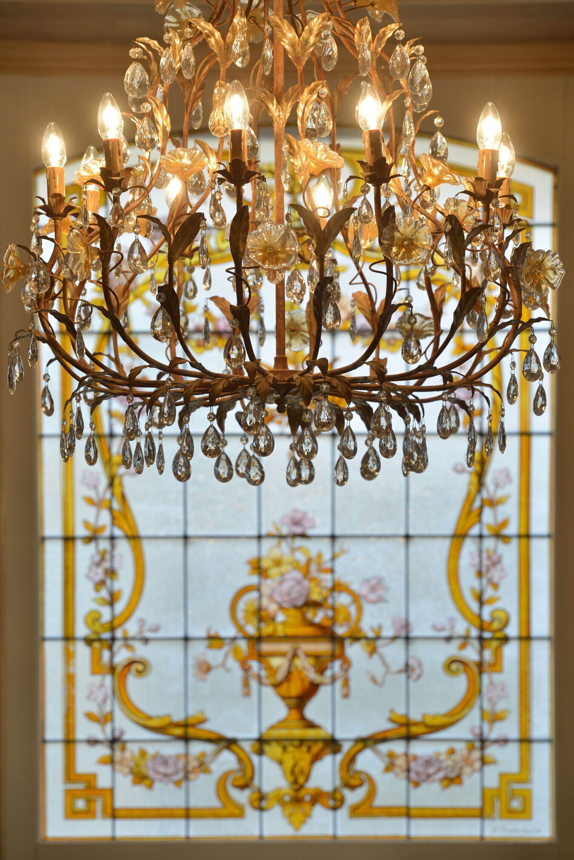 Un lustre orné de décorations et de lumières en cristal, placé devant un vitrail aux motifs floraux.