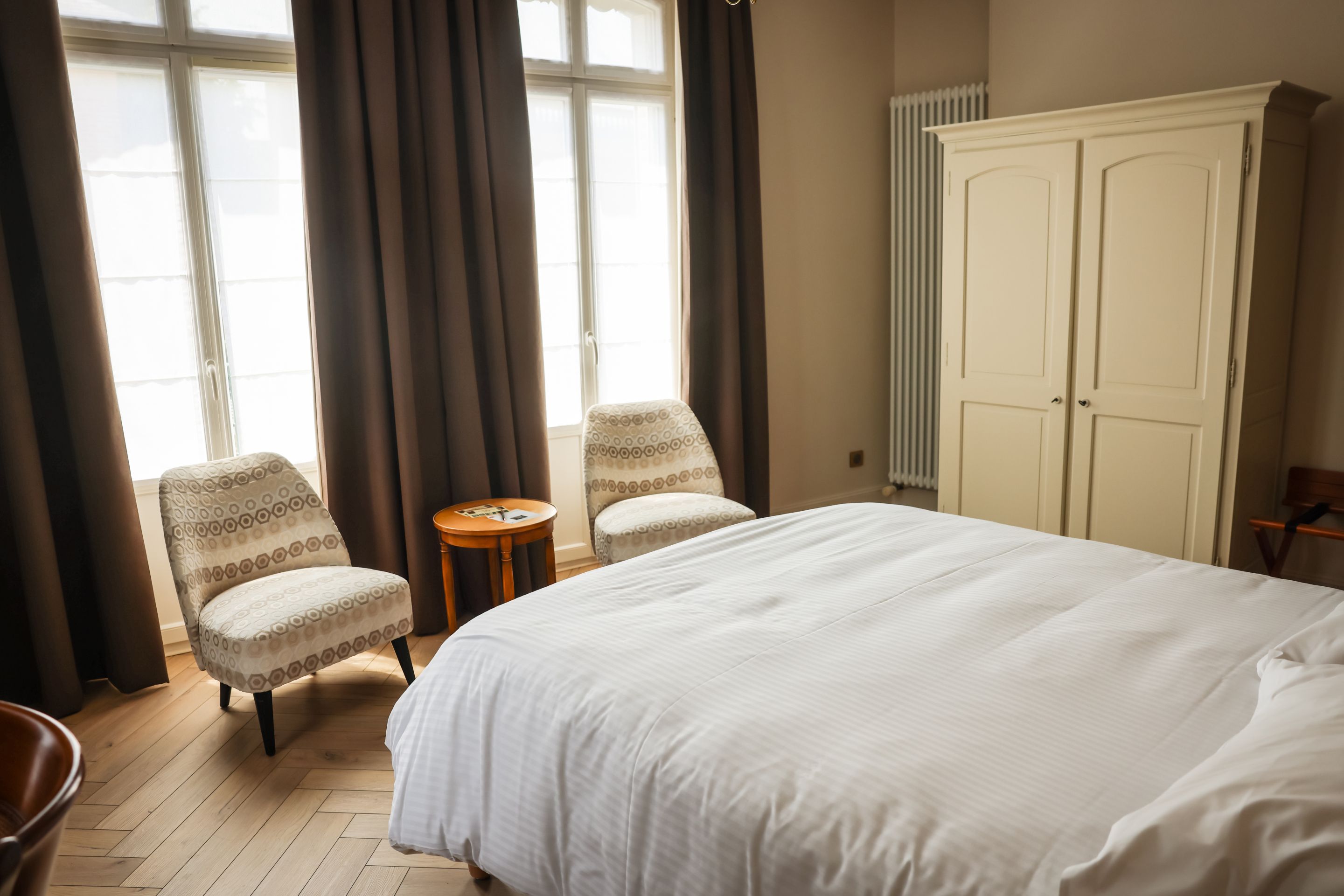 A hotel room with a large bed, two armchairs, a small table, and a wardrobe.