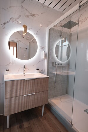 Un baño moderno con pared de mármol, un espejo redondo sobre el lavamanos y una ducha con paredes de vidrio.