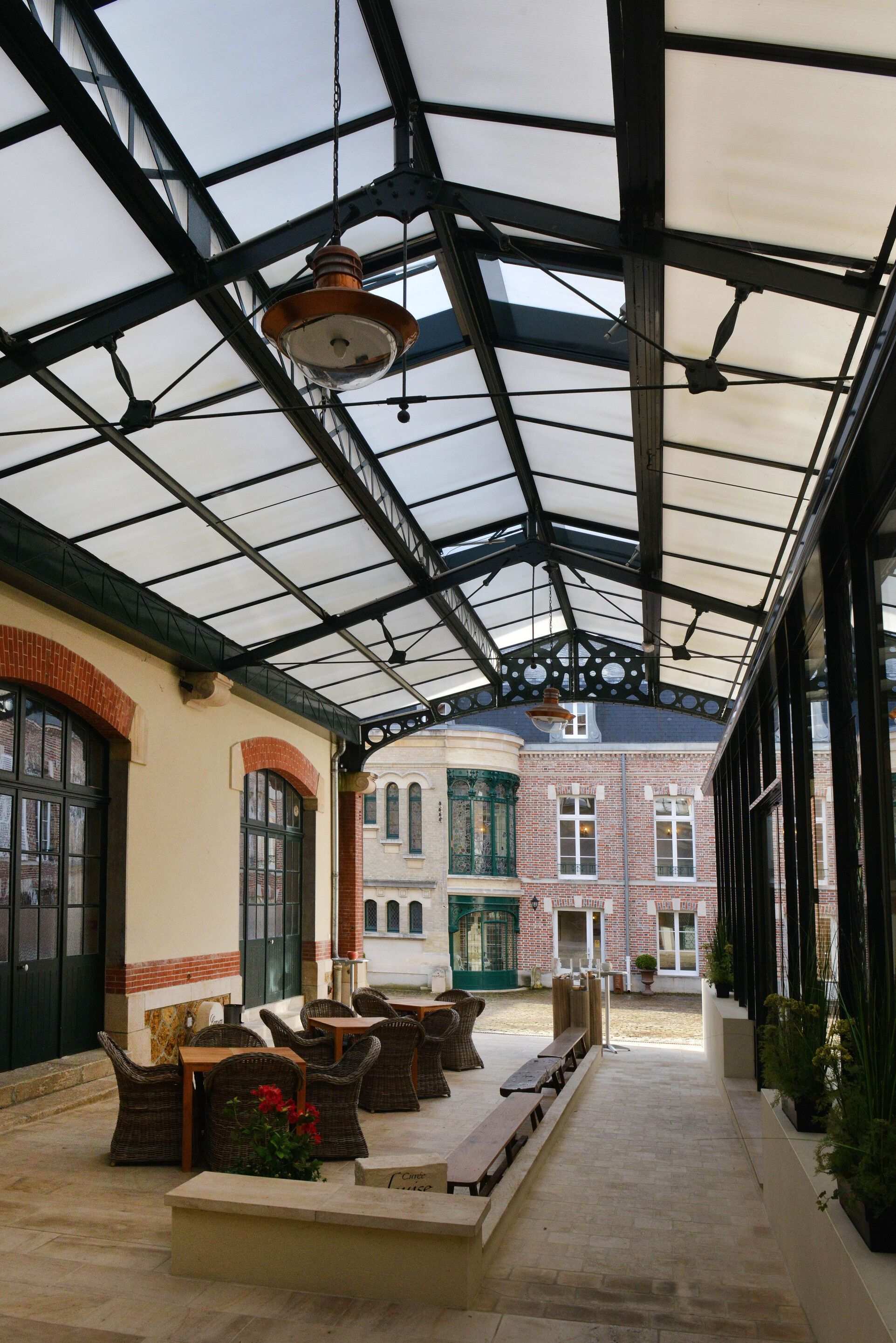A covered outdoor area with wicker furniture and a brick building in the background.