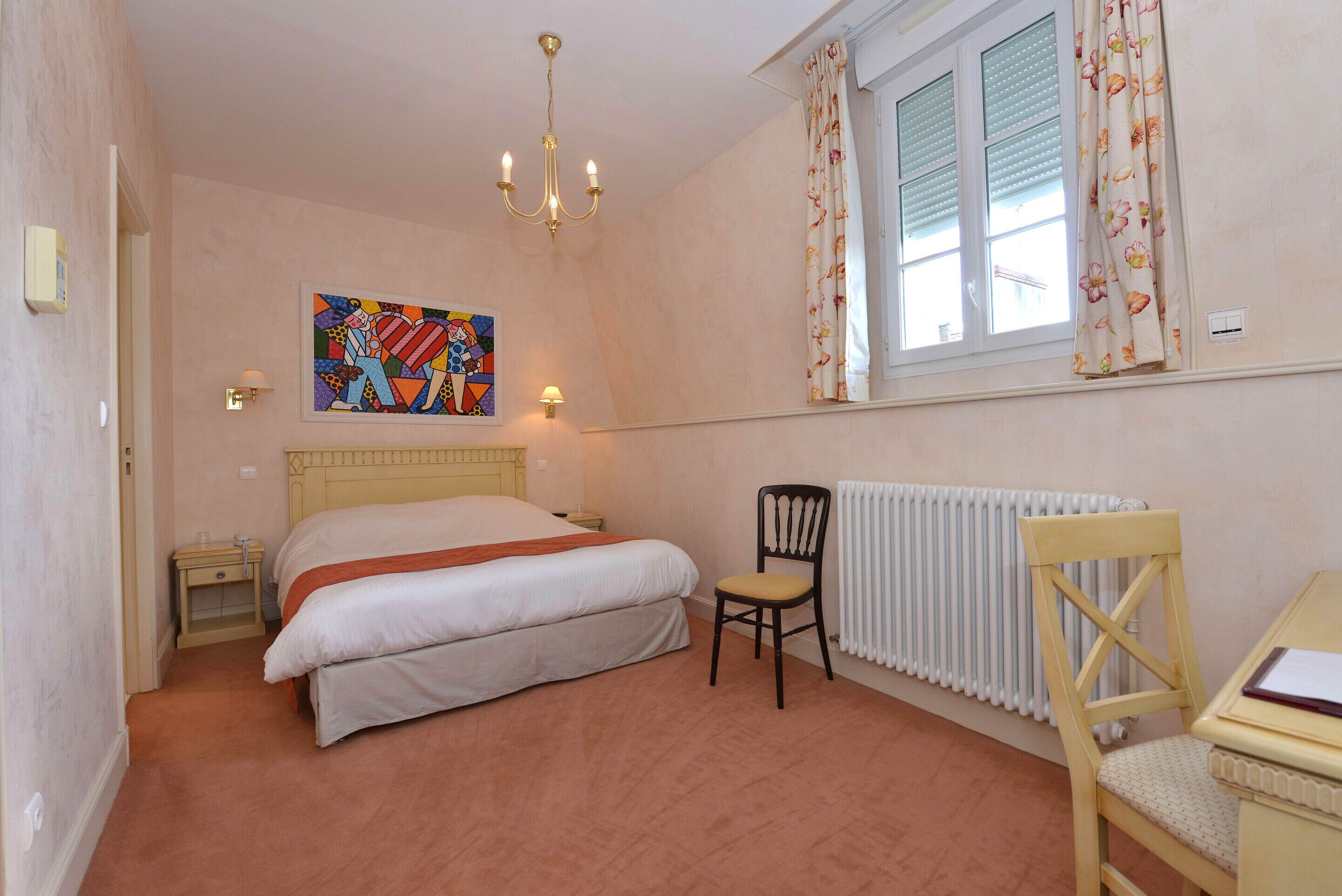 Un dormitorio con cama, una silla, un radiador, una ventana con cortinas y un cuadro en la pared.