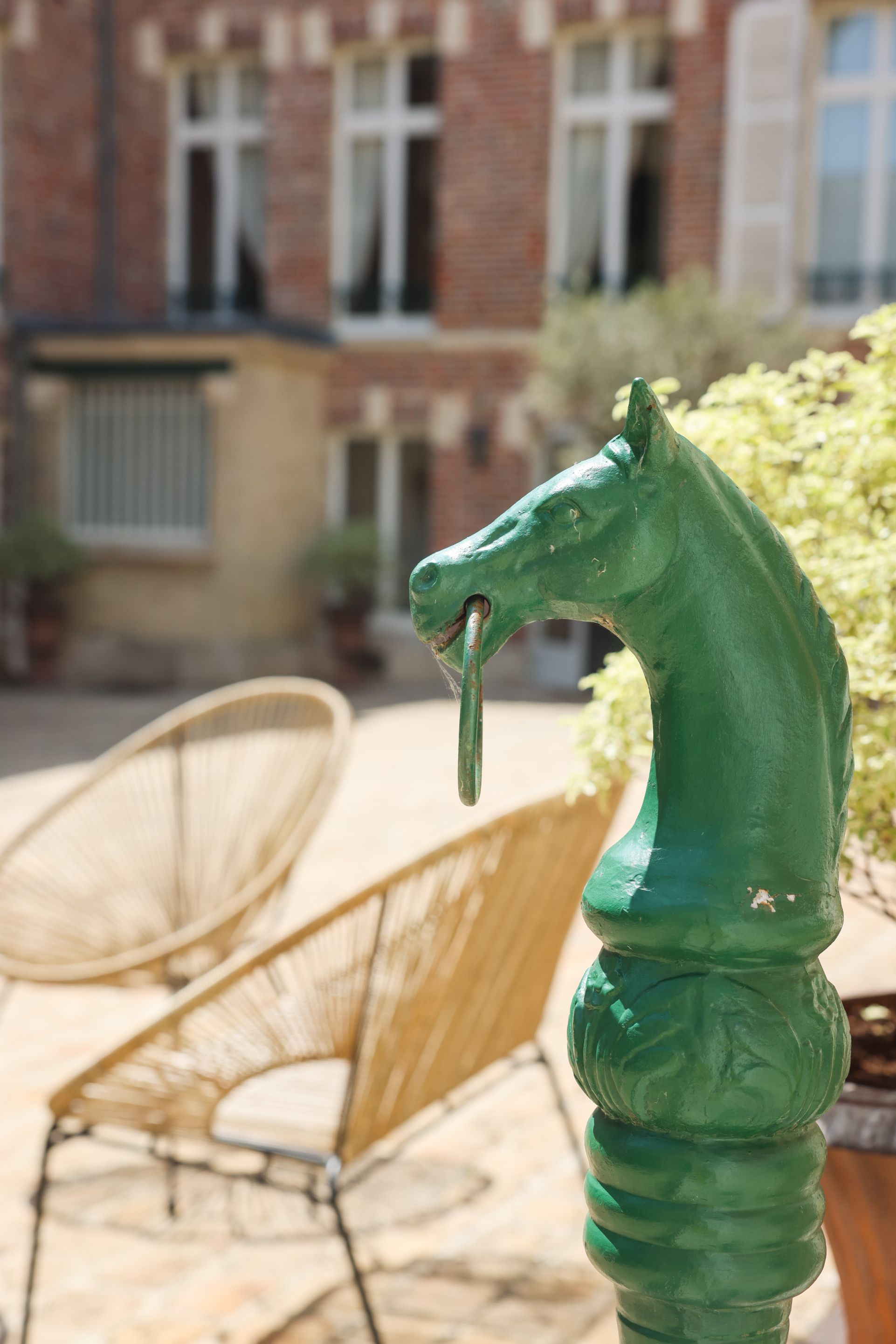 A green horse sculpture in an outdoor setting with a chair and a building in the background.